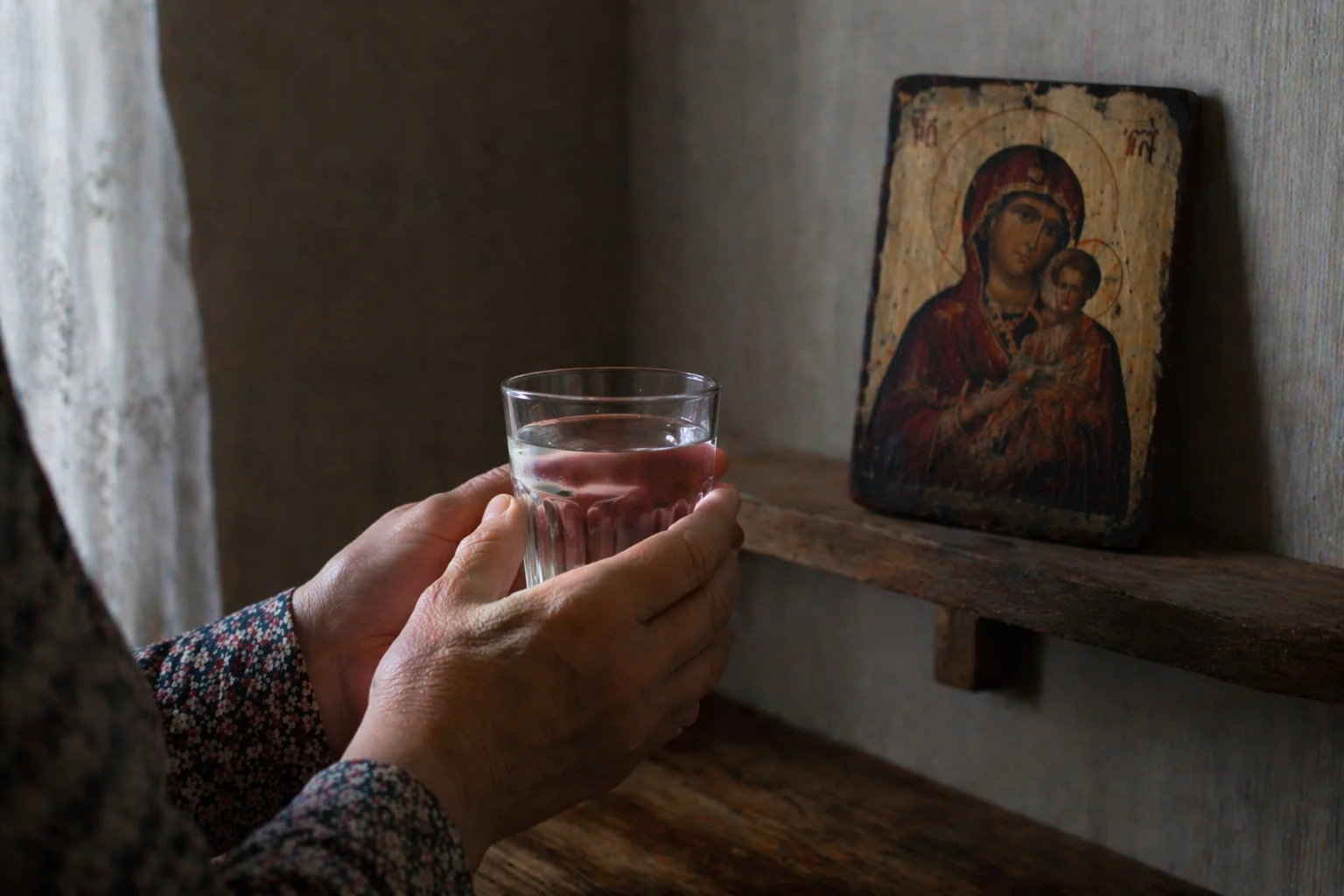 Женские руки держат стакан воды перед небольшой домашней иконой Богородицы — обряд с иконой