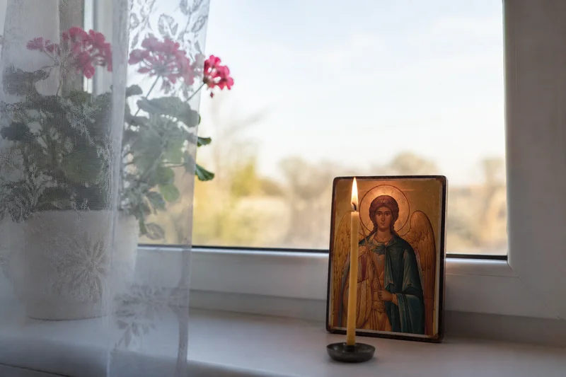 Зажжённая восковая свеча перед иконой у окна в утреннем свете — когда читать молитву Ангелу Хранителю
