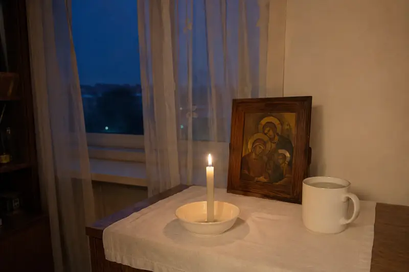 Тихий вечерний угол с иконкой и тонкой горящей свечой на льняной скатерти, в окне глубокие сумерки, маленькая чашка простой воды рядом — когда читать заговор о снятии материнского слова