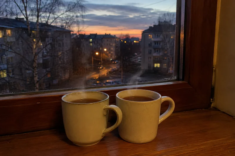 Две чашки чая на подоконнике рядом, на улице ранний вечер, тёплый домашний свет — совместимость Овна и Девы в любви и отношениях