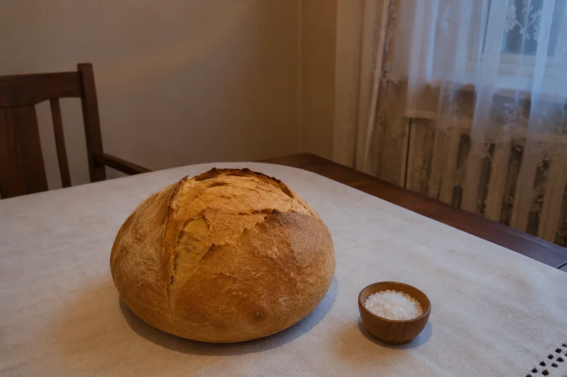 Целый домашний каравай хлеба на белой льняной скатерти, рядом солонка с крупной солью, тёплый вечерний свет от окна — над какими блюдами рождественского стола читают наговор