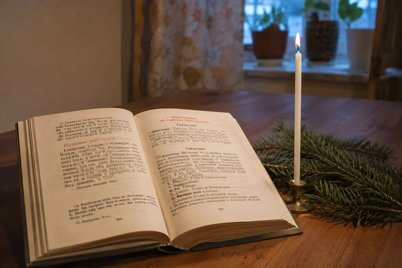 Открытая на рождественской странице книга-молитвослов на столе рядом с тонкой свечой и веточкой ели, тёплый вечерний свет — какие молитвы читают в Рождество о семье