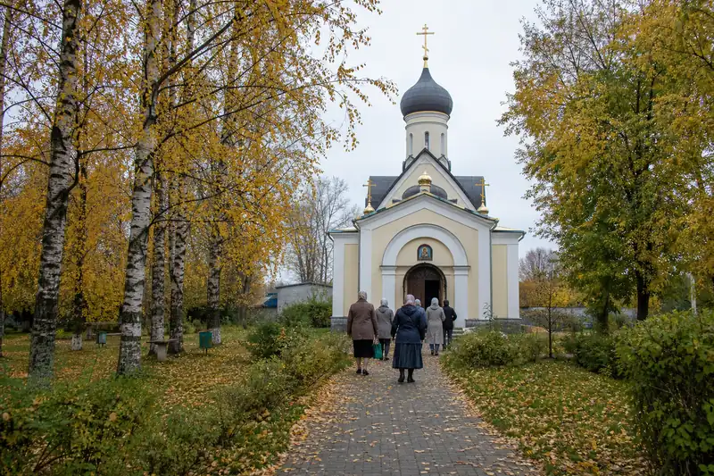 Небольшой православный храм среди осенних берёз и прихожане со спины у входа — смысл праздника Покрова Пресвятой Богородицы