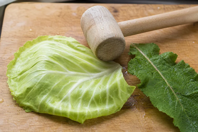 Капустный лист и деревянный молоток для отбивания на кухонной разделочной доске — какие листья кладут на ноги при варикозе
